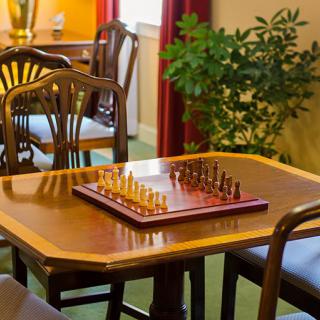 A wooden table with a chessboard set up, surrounded by chairs in an indoor setting.