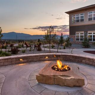 A scenic outdoor patio with a fire pit at sunset, overlooking mountains and adjacent to a building.
