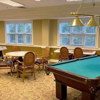 A recreation room featuring a pool table, tables, and chairs with ample lighting and windows.