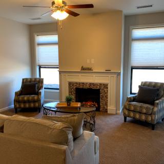 A cozy living room featuring a fireplace, comfortable seating, and natural light from large windows.
