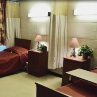 A shared hospital room with two beds and bedside tables, illuminated by lamps.