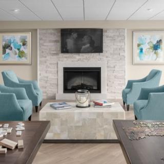 A modern living room with a fireplace, surrounded by blue armchairs, and adorned with artwork and a television.