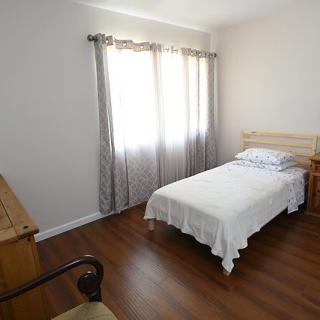 A minimalist bedroom featuring a single bed with white bedding and wooden furniture.