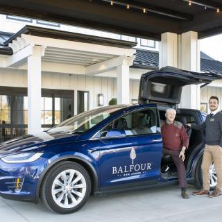 Two people standing next to a Tesla with 'Balfour' branding in front of a building entrance.