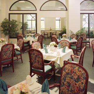 An elegantly decorated dining area with multiple tables set for guests, featuring floral-patterned chairs and indoor plants.