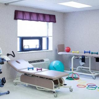 A physical therapy clinic room equipped with various rehabilitation tools, including a treatment table, exercise ball, and dumbbells.