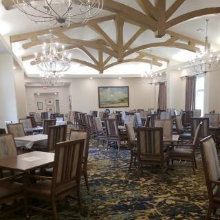 An elegantly designed dining room with multiple wooden tables and chairs, decorated with chandeliers and wooden ceiling beams.
