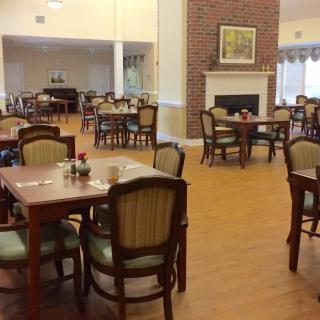 A spacious dining area with several tables and chairs, featuring a cozy fireplace and wooden flooring.