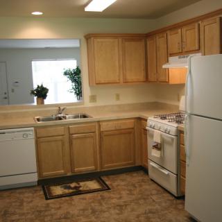 A modern kitchen with wooden cabinets, white appliances, and a tiled floor.