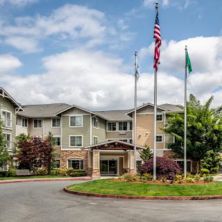 A residential building with flags in front, surrounded by trees and landscaping under a cloudy sky.