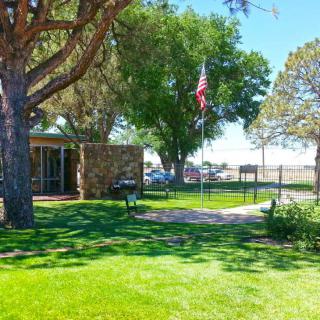 A sunny day in a park with lush green grass, trees, and an American flag near a small building.
