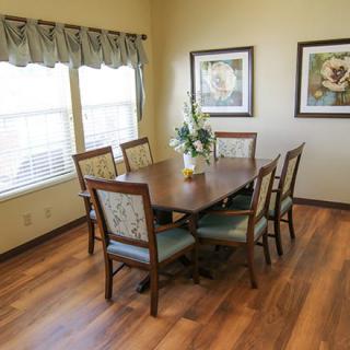 A cozy dining room featuring a wooden table and six chairs, adorned with floral decorations and two pieces of artwork on the wall.