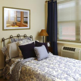 A cozy bedroom with a neatly made bed, decorated pillows, and a framed painting on the wall.