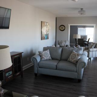 A modern living room with a cozy sofa, wall-mounted TV, and dining area in the background.
