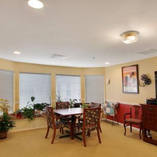 A cozy dining area with a table and chairs, surrounded by large windows and decorated with plants and artwork.