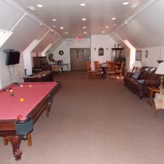A spacious game room featuring a pool table with red cloth, comfortable seating, a television, and a well-lit atmosphere.