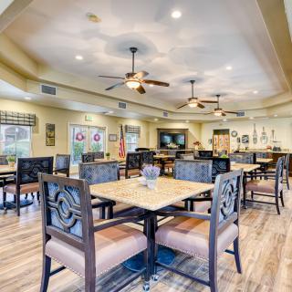 A spacious dining area with multiple tables and chairs, featuring ceiling fans and wooden flooring.