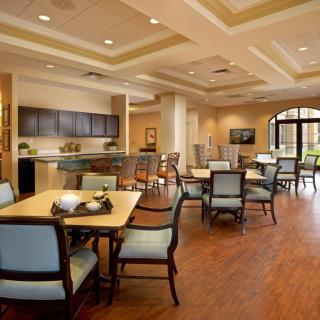 A spacious dining area with multiple tables and chairs, featuring a wooden floor and ceiling lights.