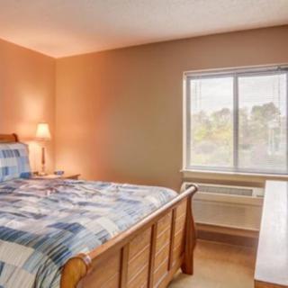 A cozy bedroom with a wooden bed, patterned bedding, a lamp, and a window.