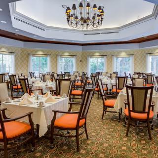 An elegant dining room with neatly arranged tables and chairs, featuring white tablecloths and a chandelier overhead.