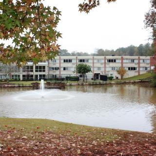 A scenic view of a building by a lake with a fountain and autumn foliage.