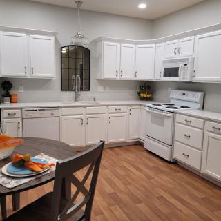 A modern kitchen with white cabinets, a dining table, and wood flooring.