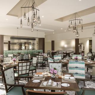 An elegant restaurant dining room with neatly arranged tables and chairs, featuring stylish chandeliers.