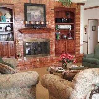 A cozy living room featuring a brick fireplace, comfortable seating, and decorative shelves.