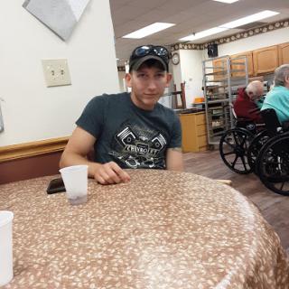 A man sitting at a table in a community center, surrounded by people in wheelchairs.