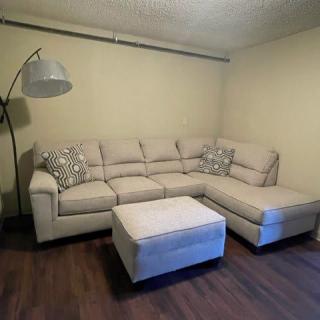 A cozy living room setup featuring a beige sectional sofa and matching ottoman with a floor lamp.