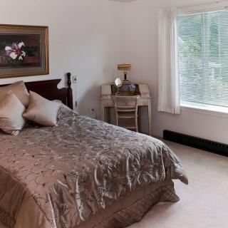 A cozy bedroom interior featuring a neatly made bed, a vintage-style vanity, and a large window providing natural light.
