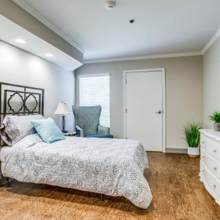 A neatly arranged bedroom with a bed, chair, and dresser on a wooden floor.