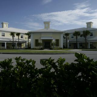 A modern building surrounded by palm trees and greenery under a partly cloudy sky.