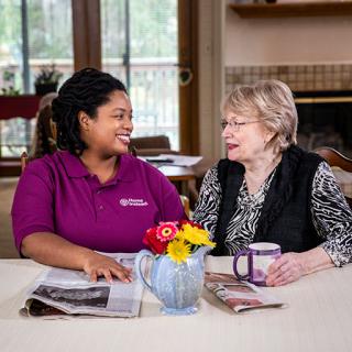 A caregiver shares a warm moment with a senior, enjoying coffee and conversation at home.