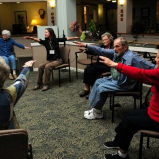 A group of seniors participating in a seated exercise class indoors.