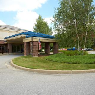 A welcoming entrance to a modern building, surrounded by greenery and a clear sky.