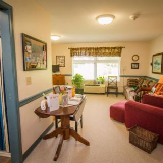 A cozy living room with a table and chairs, a sofa, and large windows adorned with curtains.