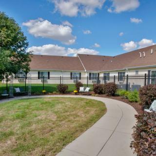 A well-maintained outdoor area with a curved pathway, lawn, and shrubs next to a building under a partly cloudy sky.