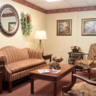 A cozy living room with a striped sofa, armchairs, and a wooden coffee table, featuring decorative elements like a wall mirror and paintings.