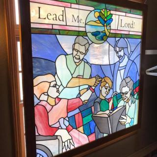 A stained glass window depicting a religious scene with the text 'Lead Me, Lord'.