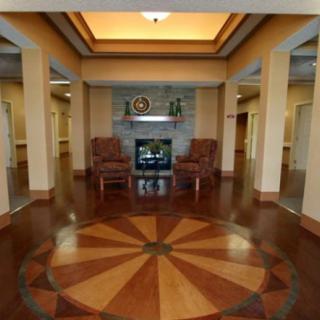 A spacious lobby area featuring a central floor pattern, flanked by columns and accentuated with armchairs near a fireplace.