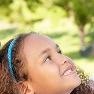 A smiling child looks upwards while enjoying a sunny day outdoors.