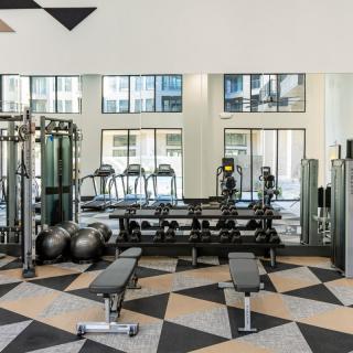 A modern gym with treadmills, weights, and benches, featuring a stylish geometric floor design.
