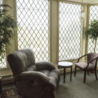 A cozy lounge area featuring a leather armchair, wooden chairs, and large windows with lattice patterns.