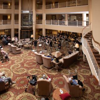 A spacious lobby with multiple seating areas, where a group of seniors are gathered, creating a warm and social atmosphere.