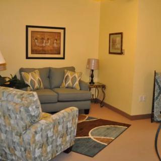 Cozy living room with a sofa and armchair, decorated with artwork and a patterned rug.