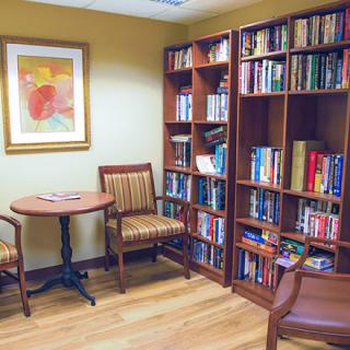 A cozy reading nook with bookshelves filled with books, a round table, and two chairs, alongside a piece of abstract art on the wall.