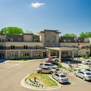 A large building with a parking lot filled with cars on a sunny day.