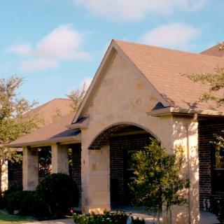 A view of a residential house with brick exterior and gabled roof, surrounded by trees.