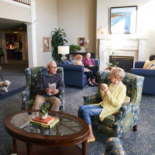 A group of seniors relaxing and conversing in a cozy living room setting with comfortable armchairs and a coffee table.